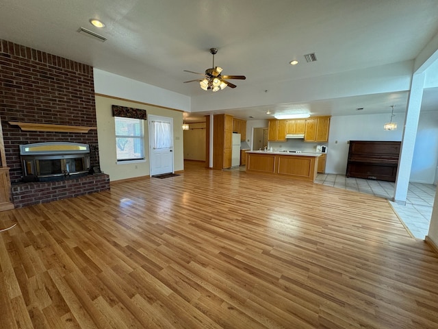 unfurnished living room with light hardwood / wood-style flooring, ceiling fan, brick wall, and a brick fireplace