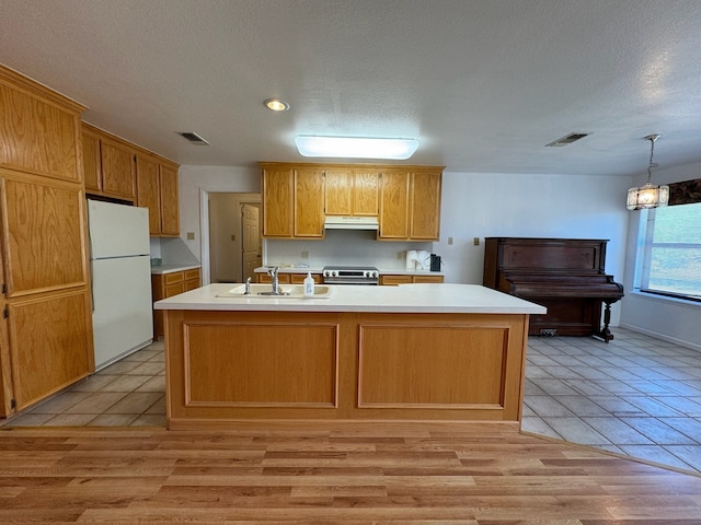 kitchen featuring sink, white refrigerator, light wood-type flooring, a kitchen island with sink, and a textured ceiling