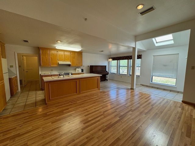 kitchen with pendant lighting, vaulted ceiling with skylight, light hardwood / wood-style floors, white fridge, and sink