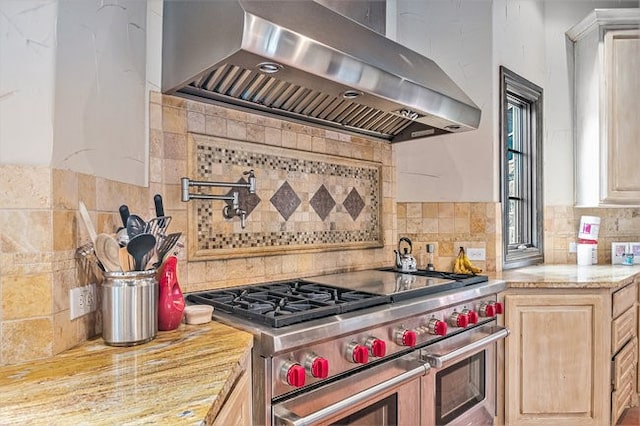 kitchen featuring wall chimney exhaust hood, light brown cabinetry, backsplash, double oven range, and light stone counters