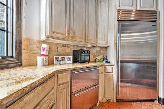 kitchen with backsplash, light brown cabinetry, tile patterned floors, light stone counters, and built in refrigerator