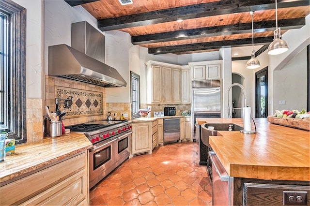 kitchen with wood counters, beamed ceiling, wall chimney exhaust hood, tasteful backsplash, and double oven range