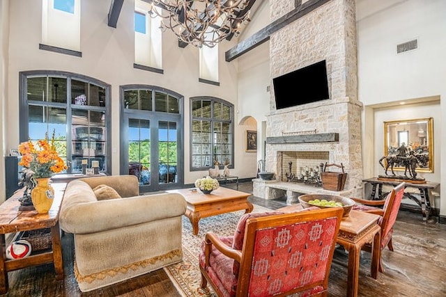 living room featuring a towering ceiling, hardwood / wood-style flooring, an inviting chandelier, and a stone fireplace