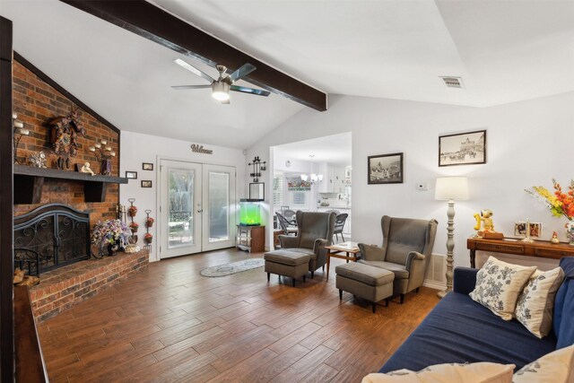 living room featuring brick wall, vaulted ceiling with beams, ceiling fan with notable chandelier, wood-type flooring, and a brick fireplace