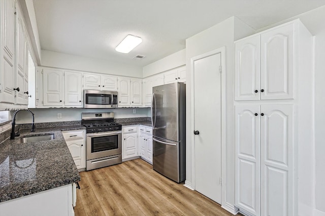 kitchen with white cabinetry, sink, dark stone counters, light hardwood / wood-style floors, and appliances with stainless steel finishes