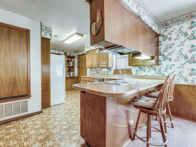 kitchen with premium range hood, kitchen peninsula, a kitchen bar, white fridge, and a textured ceiling