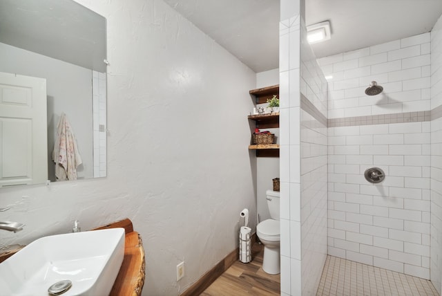 bathroom with sink, toilet, a tile shower, and hardwood / wood-style flooring