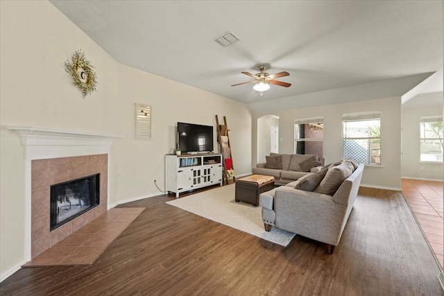 living room featuring ceiling fan, a tiled fireplace, and dark hardwood / wood-style flooring