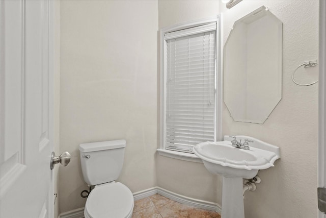 half bathroom with toilet, baseboards, and tile patterned floors