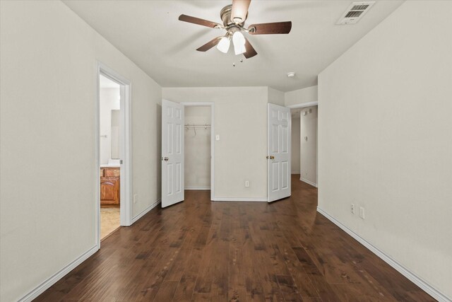 unfurnished bedroom featuring a walk in closet, dark hardwood / wood-style floors, a closet, ceiling fan, and connected bathroom