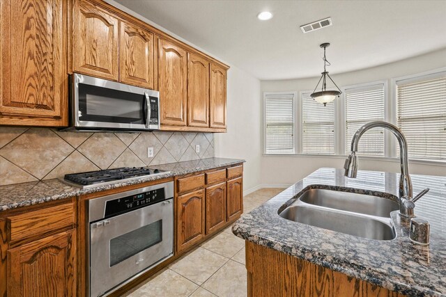 kitchen with backsplash, appliances with stainless steel finishes, light tile patterned floors, sink, and decorative light fixtures