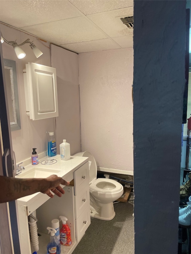 bathroom with toilet, sink, and a drop ceiling