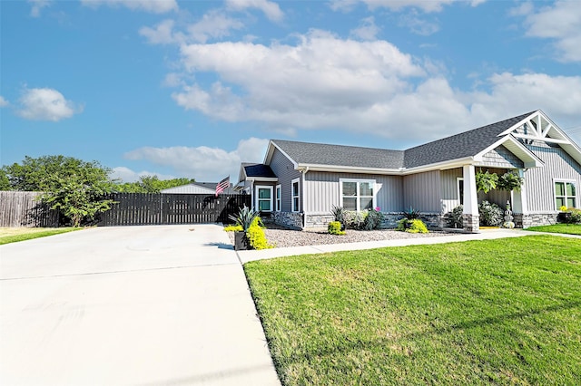 view of front of property with stone siding, roof with shingles, fence, a front lawn, and board and batten siding