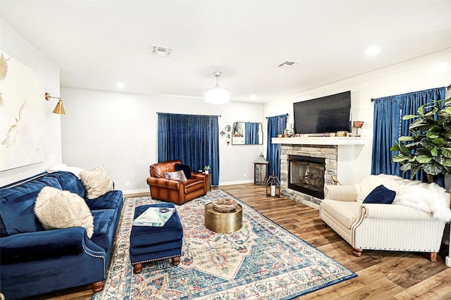 living room with visible vents, a stone fireplace, baseboards, and wood finished floors