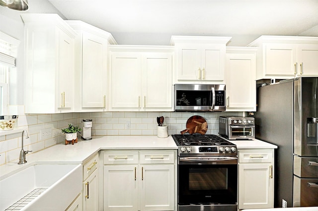 kitchen with stainless steel appliances, light countertops, decorative backsplash, white cabinetry, and a sink