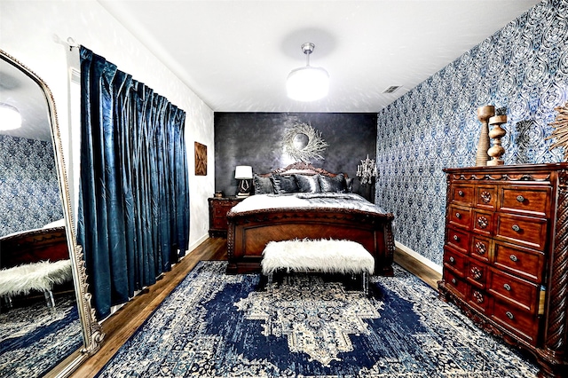 bedroom featuring wallpapered walls, visible vents, baseboards, and wood finished floors