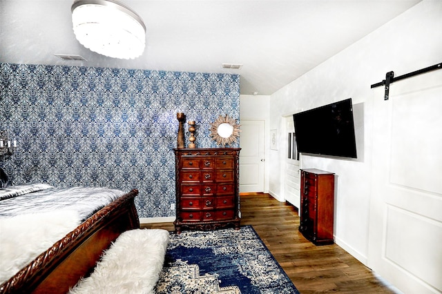 bedroom featuring a barn door, wood finished floors, visible vents, and baseboards