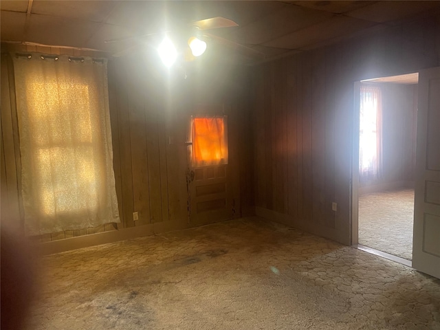 carpeted empty room featuring wood walls and ceiling fan