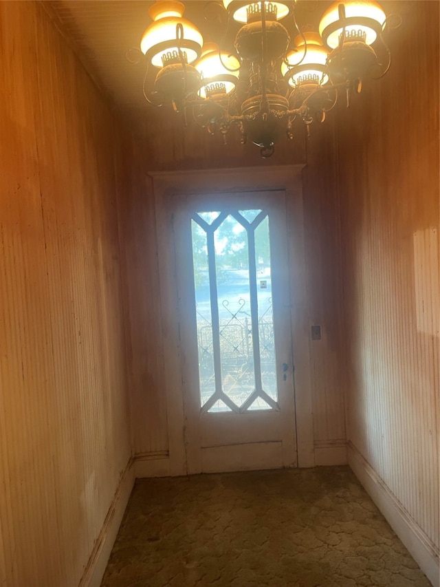 doorway featuring carpet flooring, wood walls, and a chandelier