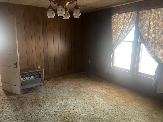 carpeted empty room with wood walls, an inviting chandelier, and heating unit