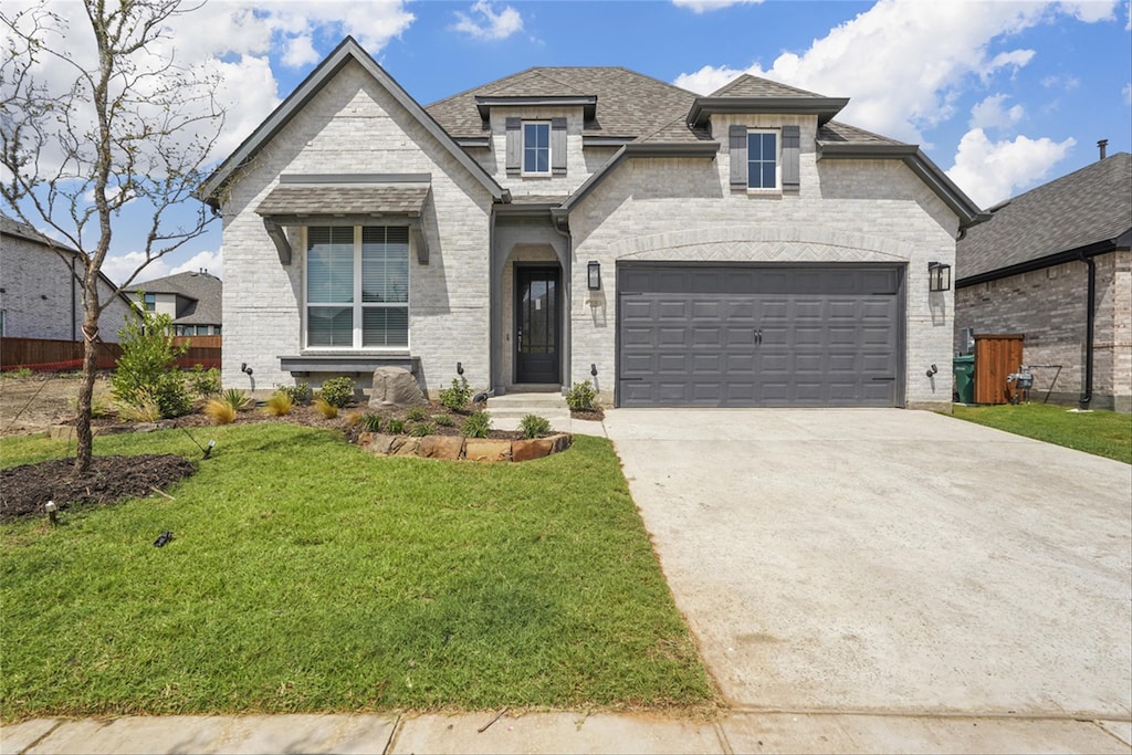 french country home featuring brick siding, concrete driveway, a front lawn, and a garage