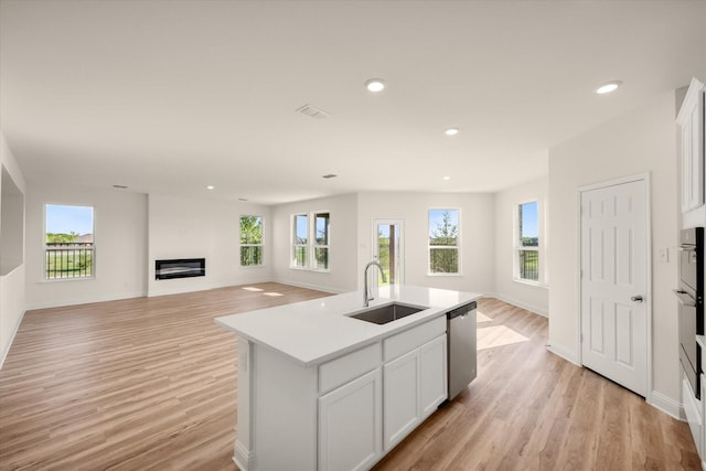 kitchen featuring sink, light hardwood / wood-style flooring, stainless steel dishwasher, a center island with sink, and white cabinets