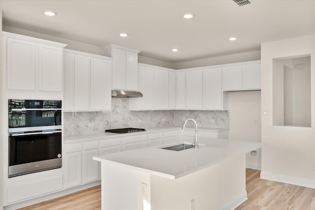 kitchen with decorative backsplash, light wood-type flooring, sink, white cabinetry, and an island with sink