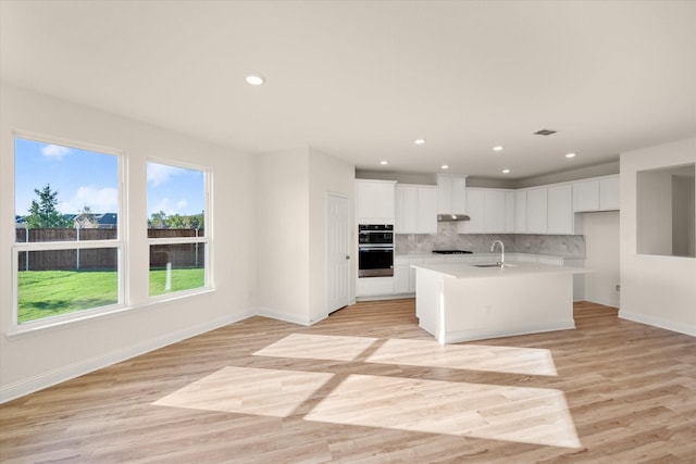 kitchen featuring white cabinets, backsplash, a center island with sink, and light hardwood / wood-style flooring