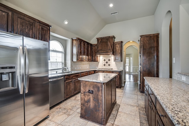 kitchen featuring light tile patterned flooring, backsplash, light stone counters, a kitchen island, and stainless steel appliances