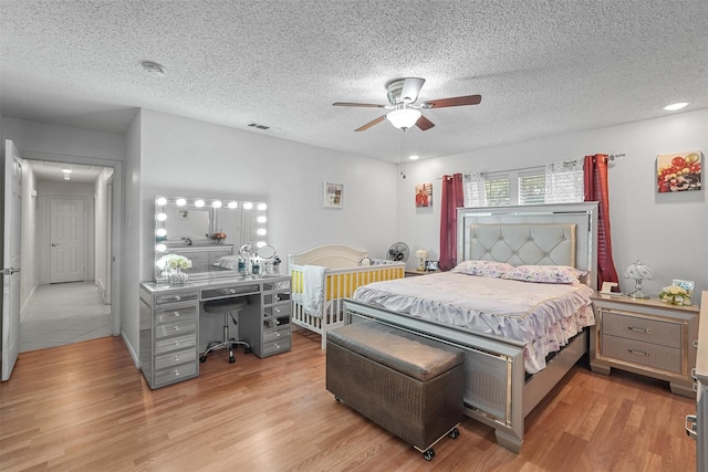 bedroom featuring visible vents, a textured ceiling, light wood-type flooring, and ceiling fan