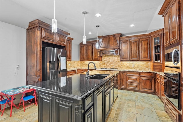 kitchen with appliances with stainless steel finishes, custom range hood, decorative backsplash, a kitchen island with sink, and dark stone counters