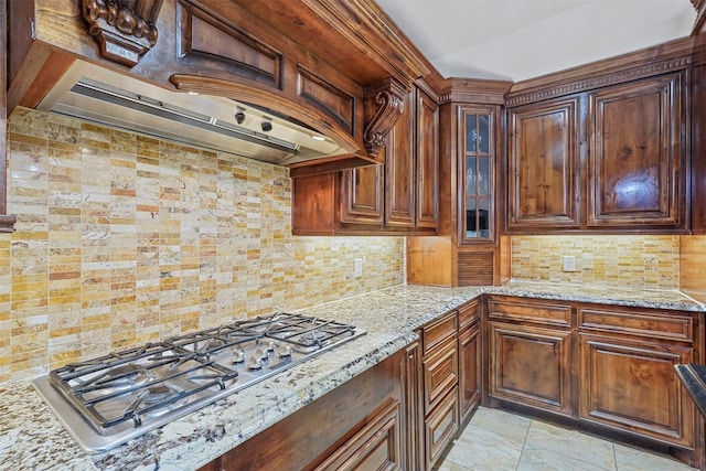 kitchen with light stone counters, backsplash, stainless steel gas stovetop, and exhaust hood