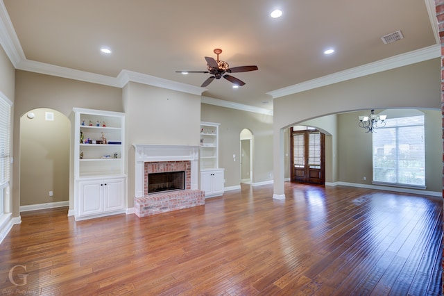 unfurnished living room featuring ceiling fan with notable chandelier, a brick fireplace, ornamental molding, and hardwood / wood-style floors