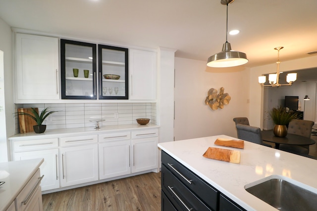 kitchen with an inviting chandelier, tasteful backsplash, pendant lighting, white cabinets, and light wood-type flooring