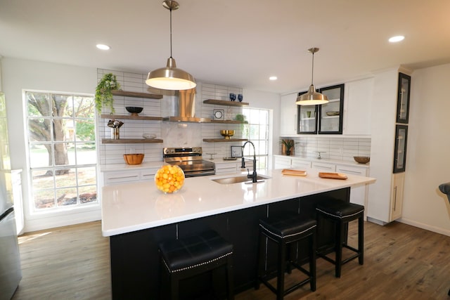 kitchen featuring electric range, sink, dark hardwood / wood-style flooring, decorative backsplash, and a center island with sink