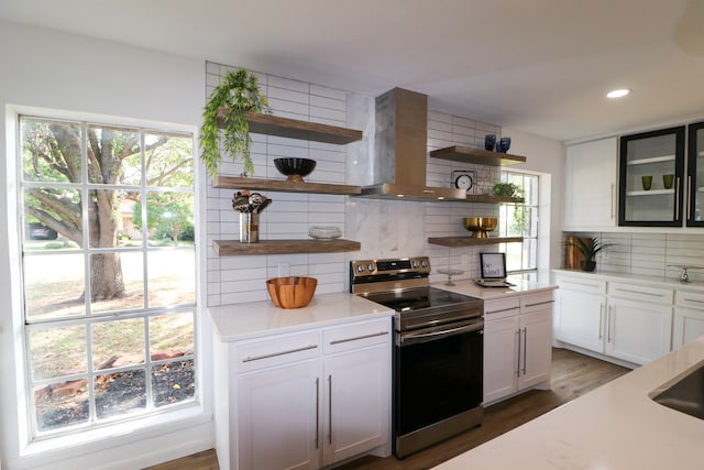 kitchen with stainless steel electric stove, white cabinets, wall chimney range hood, and backsplash