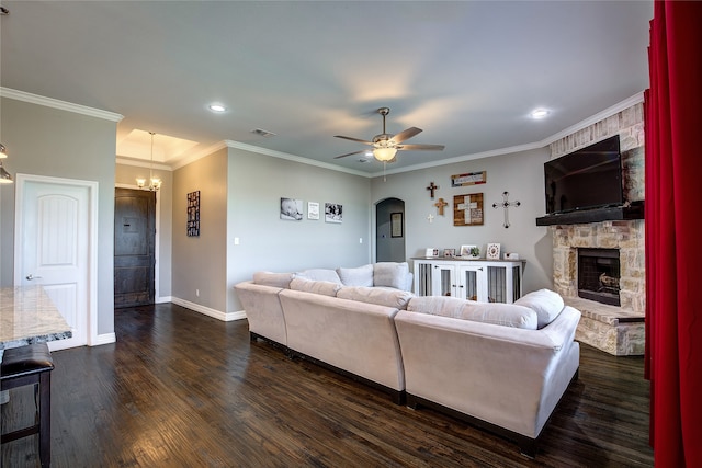 living room with ornamental molding, ceiling fan with notable chandelier, dark wood-type flooring, and a stone fireplace