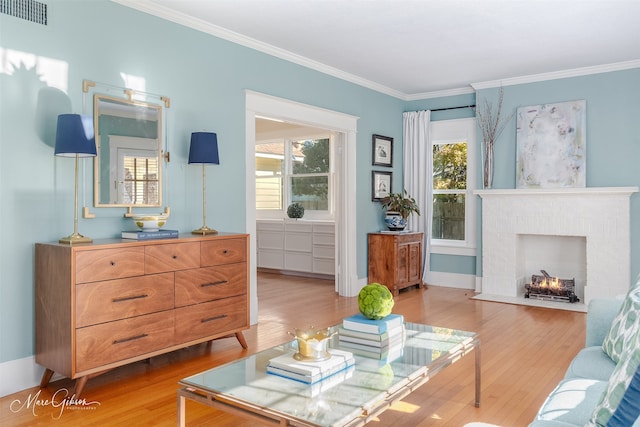 living room featuring a brick fireplace, a healthy amount of sunlight, crown molding, and light hardwood / wood-style flooring