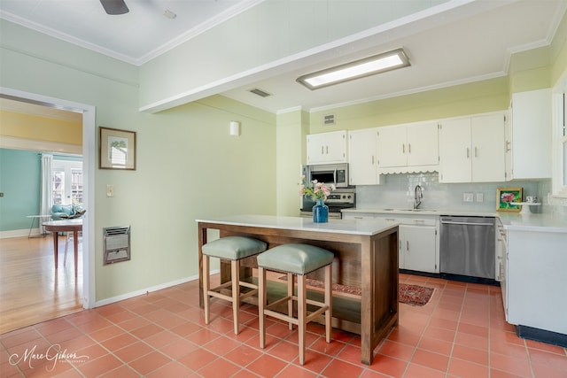 kitchen with tasteful backsplash, stainless steel appliances, sink, white cabinets, and a kitchen island