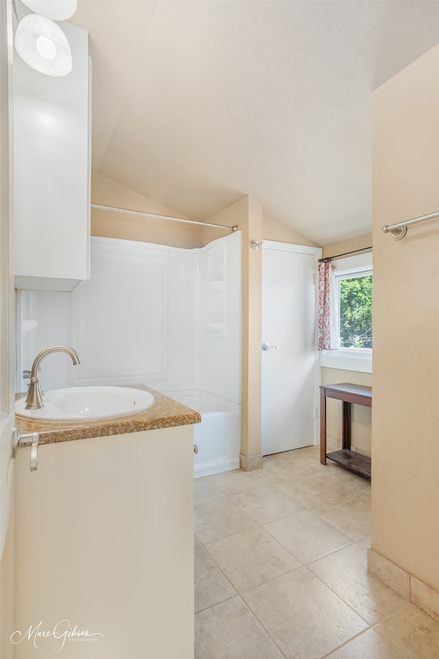 bathroom with tile patterned flooring, vaulted ceiling, walk in shower, and sink