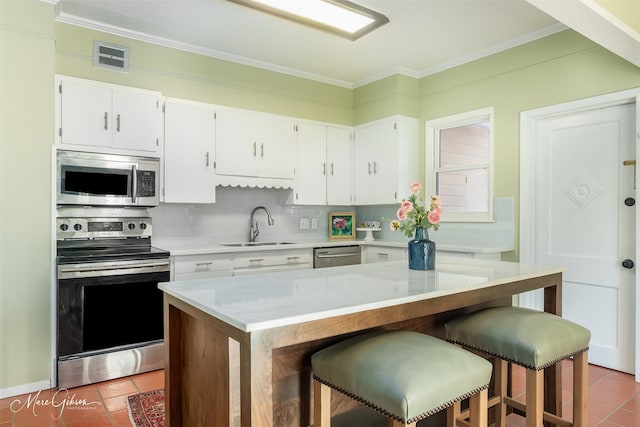 kitchen with sink, backsplash, a breakfast bar area, white cabinets, and appliances with stainless steel finishes