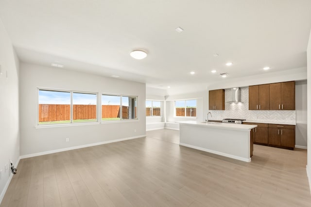 kitchen featuring a kitchen island with sink, wall chimney range hood, sink, light hardwood / wood-style flooring, and decorative backsplash