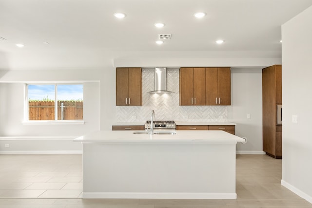 kitchen with decorative backsplash, sink, wall chimney exhaust hood, and a center island with sink