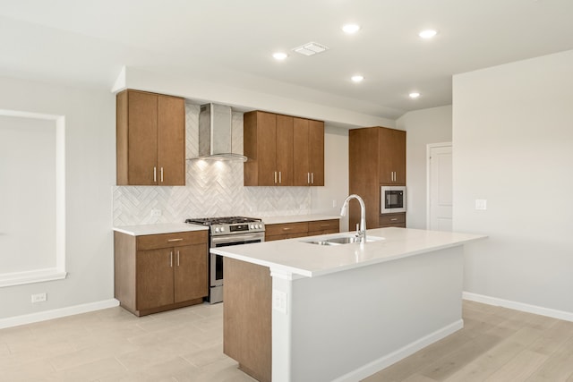 kitchen with stainless steel range with gas cooktop, sink, wall chimney exhaust hood, and an island with sink