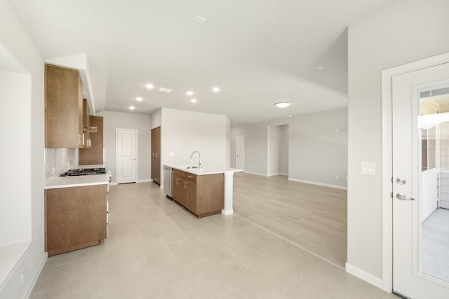 kitchen featuring decorative backsplash, wall chimney exhaust hood, sink, dishwasher, and an island with sink