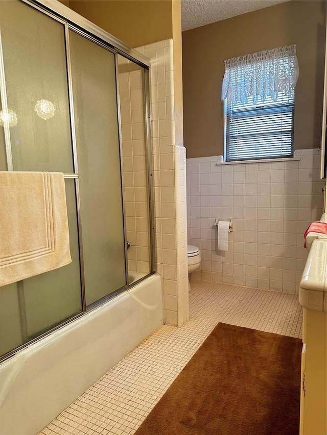 full bath with combined bath / shower with glass door, tile walls, toilet, and tile patterned floors