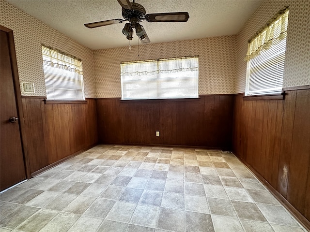 unfurnished room featuring wooden walls, ceiling fan, and a textured ceiling