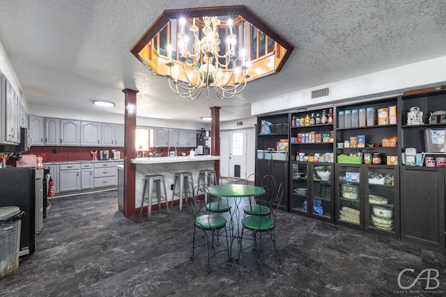 tiled dining space featuring a textured ceiling, a notable chandelier, and decorative columns