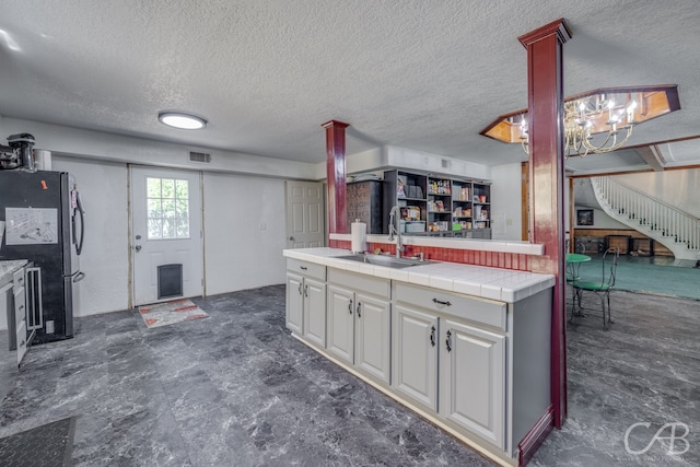 kitchen featuring stainless steel refrigerator, white cabinetry, tile countertops, sink, and dark tile patterned flooring