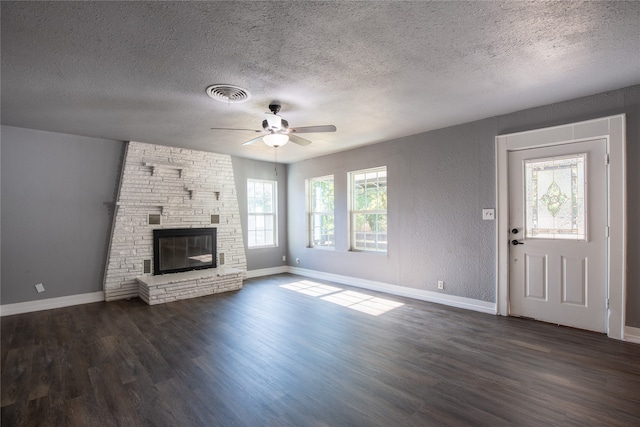 unfurnished living room with a stone fireplace, ceiling fan, a textured ceiling, and dark hardwood / wood-style flooring